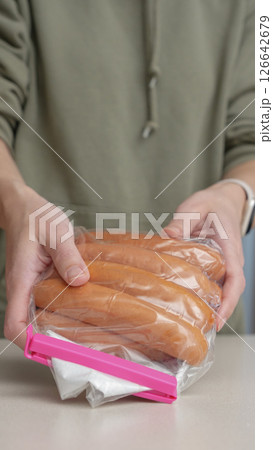 Hands covering open sausage bag with food clip for storage. Meat sausage in a package for long-term storage. Hands covering open sausage bag with food clip for storage. Meat sausage in a package for long-term storage. 126642679