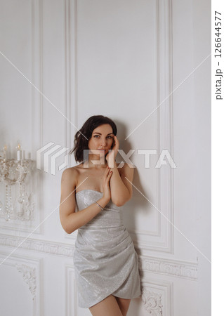 Young woman in silver dress posing against white classic wall in elegant room 126644577
