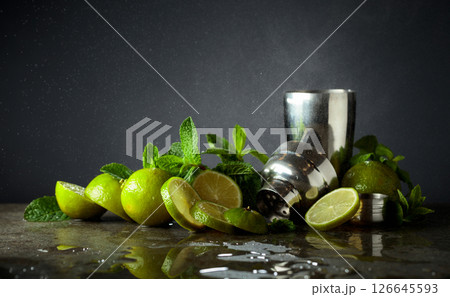 Shaker, limes, and fresh mint branches on a stone table. Shaker, limes, and fresh mint branches on a stone table. 126645593