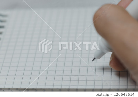 Woman Hand's Writing on a Grid Notebook with a White Pen Woman Hand's Writing on a Grid Notebook with a White Pen 126645614