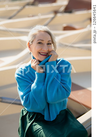 Gray-haired woman in a blue sweater against the background of boats, a lake and a forest in the Versailles park 126645641