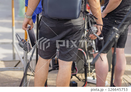Men holding drone and tablet at an outdoor event. Drone operators preparing for an aerial shoot, showcasing modern technology in video production, event coverage Men holding drone and tablet at an outdoor event. Drone operators preparing for an aerial shoot, showcasing modern technology in video production, event coverage 126645753