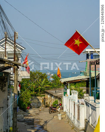 Vietnamese coastal alleyway with flags, with a glimpse of the sea and boats in the sunny background Vietnamese coastal alleyway with flags, with a glimpse of the sea and boats in the sunny background 126646966