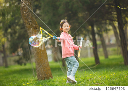 Happy Girl Blowing Large Soap Bubbles in Park on Summer Day Happy Girl Blowing Large Soap Bubbles in Park on Summer Day 126647308