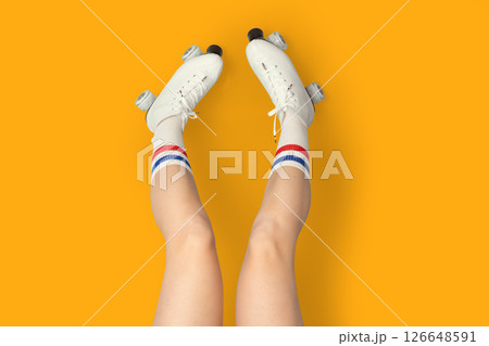 Roller skating fun with retro white skates and striped socks on vibrant orange background 126648591