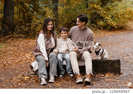 Happy family of three with dog sitting on bench in autumn park 126649987