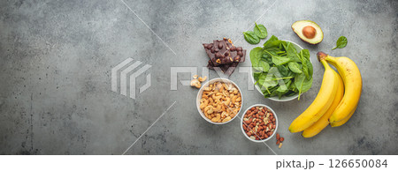 Magnesium rich foods including bananas, spinach, peanuts, cashews, and dark chocolate top view 126650084