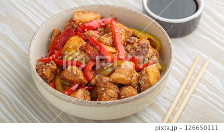 Asian stir fry chicken with red and green peppers and sesame seeds in bowl with chopsticks and soy sauce angle view on white wooden table Asian stir fry chicken with red and green peppers and sesame seeds in bowl with chopsticks and soy sauce angle view on white wooden table 126650111