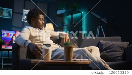 Casual person opening his laptop at home to solve daily tasks on his couch, doing remote freelance work online. Young black man surfing the web multitasking in loft apartment, tech savvy. Camera B. Casual person opening his laptop at home to solve daily tasks on his couch, doing remote freelance work online. Young black man surfing the web multitasking in loft apartment, tech savvy. Camera B. 126653339