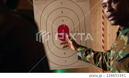 Army leader teaches recruits in shooting gallery how to shoot target center, training accuracy. Military officer instructs soldiers how to hit bullseye, explaining shooting practices, camera A closeup 126653341