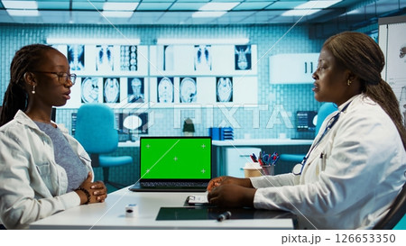 Doctor and patient discuss about health care recovery next to mockup screen, meeting in cabinet to share advice and medicine. Professional medic consulting girl during routine checkup. Camera B. 126653350