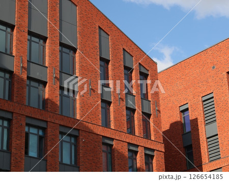 A modern brick building featuring large windows, set against a backdrop of clear skies 126654185