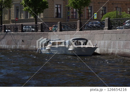 A Serene Boat Floating Gently by the Riverbank in an Urban Setting with Scenic Views A Serene Boat Floating Gently by the Riverbank in an Urban Setting with Scenic Views 126654216
