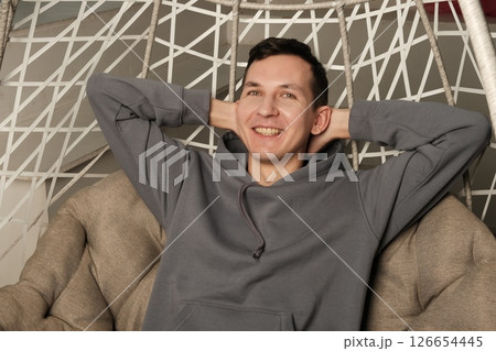 A man is sitting comfortably in a modern chair, exuding joy and radiating a cool, relaxed attitude 126654445