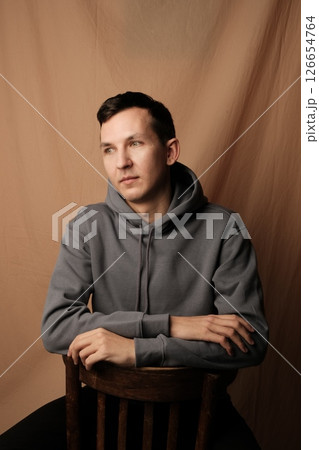 A Contemplative Young Man Dressed in a Casual Hoodie Sitting Comfortably on a Chair A Contemplative Young Man Dressed in a Casual Hoodie Sitting Comfortably on a Chair 126654764