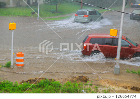 Cars drive through flooded city streets during intense rainfall, showcasing impact of severe weather on urban areas. 126654774