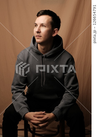 A Thoughtful and Contemplative Young Man Wearing a Casual Hoodie in a Studio Setting 126654791