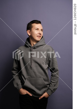 A trendy young man in a stylish hoodie strikes a cool pose against a purple background A trendy young man in a stylish hoodie strikes a cool pose against a purple background 126654820