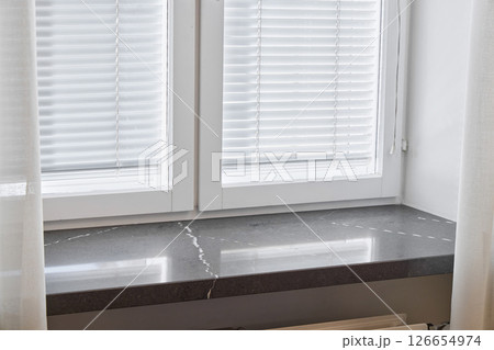 An Elegant Window Sill adorned with Modern Blinds that invite Natural Light into the room An Elegant Window Sill adorned with Modern Blinds that invite Natural Light into the room 126654974