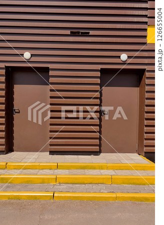 two brown doors on striped building yellow accents and concrete steps. close-up. two brown doors on striped building yellow accents and concrete steps. close-up. 126655004