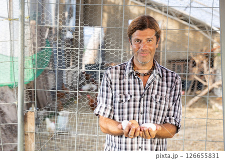 Positive male owner of farm company stands and holds in hands palms few fresh chicken eggs Positive male owner of farm company stands and holds in hands palms few fresh chicken eggs 126655831