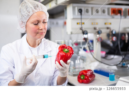Middle-aged female scientist checking vegetables for harmful elements, injecting syringe into bell pepper in laboratory Middle-aged female scientist checking vegetables for harmful elements, injecting syringe into bell pepper in laboratory 126655933