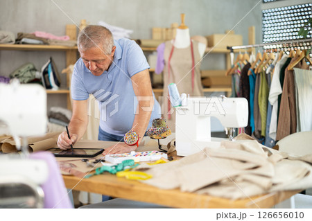 Senior man tailor creates sketch of dress on tablet Senior man tailor creates sketch of dress on tablet 126656010