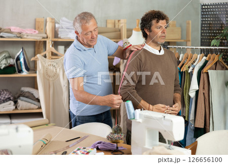 Senior man tailor takes measurements from senior male client 126656100