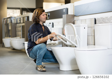 in plumbing department, male buyer checks for defects of toilet before purchasing toilet pan 126656102