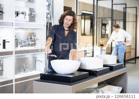 in plumbing department,thoughtful man inspects round white ceramic sinks with faucets in plumbing department,thoughtful man inspects round white ceramic sinks with faucets 126656111