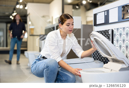 in plumbing department, female buyer checks for defects of toilet before purchasing toilet pan 126656120