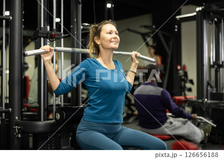 Caucasian woman doing exercises on lat pull down machine in gym 126656188