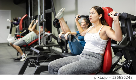 Woman is engaged in sports sitting on simulator in the gym. Woman strengthens muscles of hands on simulator Woman is engaged in sports sitting on simulator in the gym. Woman strengthens muscles of hands on simulator 126656248