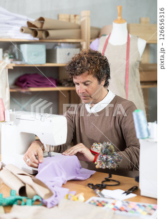 Man tailor sews on sewing machine in workshop 126656316