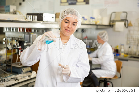 Female chemist working in laboratory, analyzing liquid samples in test flasks Female chemist working in laboratory, analyzing liquid samples in test flasks 126656351