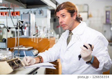 Male scientist engaged in research in chemical laboratory, noting results in chart 126656354