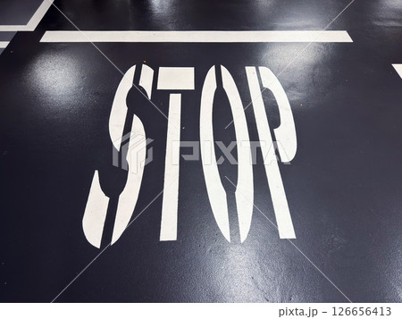 Bold white stop sign on dark asphalt surface in parking lot with clear lines 126656413