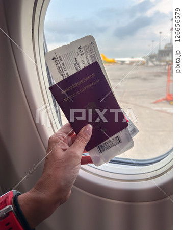 Holding a passport and boarding pass by the window on a flight 126656579