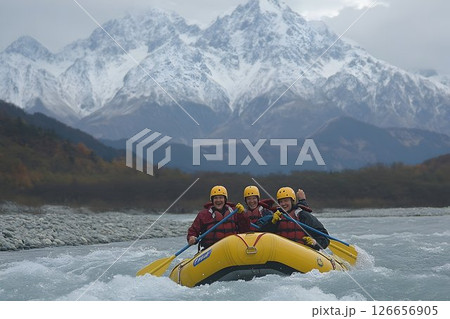 Adventurous rafting expedition: Group navigating river rapids with mountain backdrop 126656905