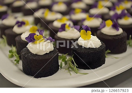 Miniature chocolate cakes adorned with whipped cream and edible flowers 126657923
