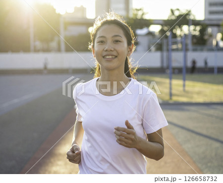 夕暮れの運動場を爽やかな笑顔で走る女性のランニングシーン 126658732