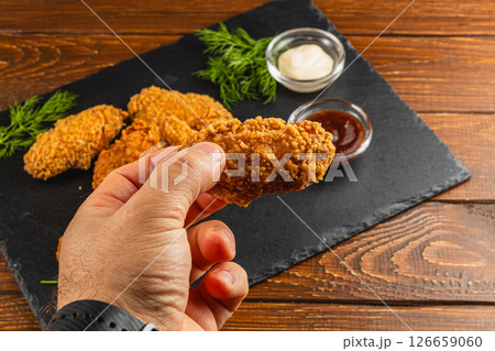 Fried chicken wing held in hand with dipping sauces on the side Fried chicken wing held in hand with dipping sauces on the side 126659060