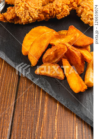 Crispy fried chicken and golden potato wedges served on slate 126659074