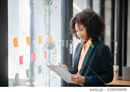 Secretary working in modern office in skyscraper, writing and sticking adhesive notes with tasks on window modern office Secretary working in modern office in skyscraper, writing and sticking adhesive notes with tasks on window modern office 126659698