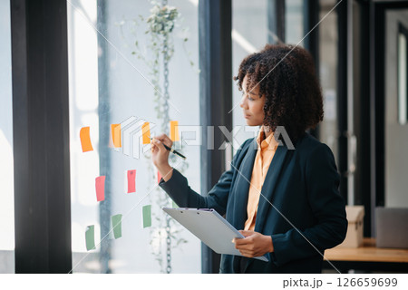 Secretary working in modern office in skyscraper, writing and sticking adhesive notes with tasks on window modern office 126659699