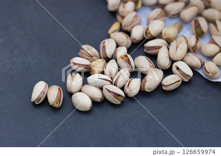 Open pistachio nuts scattered on dark surface 126659974