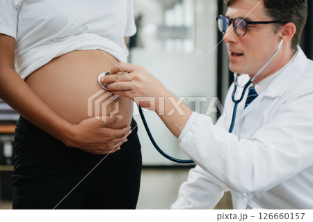 Pregnant african woman has appointment with doctor at clinic. Male gynaecologist OB GYN medic specialist with stethoscope listens to baby's heartbeat in mother's belly. Pregnant african woman has appointment with doctor at clinic. Male gynaecologist OB GYN medic specialist with stethoscope listens to baby's heartbeat in mother's belly. 126660157