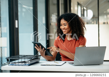 Young woman typing on tablet and laptop while sitting at the working in office 126660231