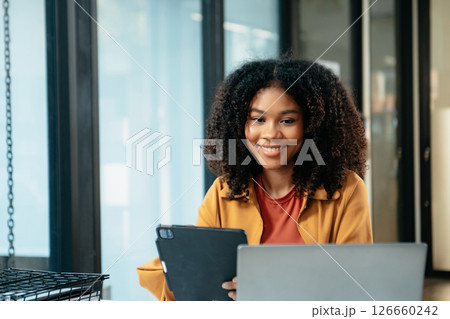 Young woman typing on tablet and laptop while sitting at the working in office 126660242