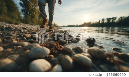 Person Walking Along Rocky Riverbank at Sunset 126660490